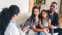 Young family sitting on sofa talking to a female doctor using digital tablet